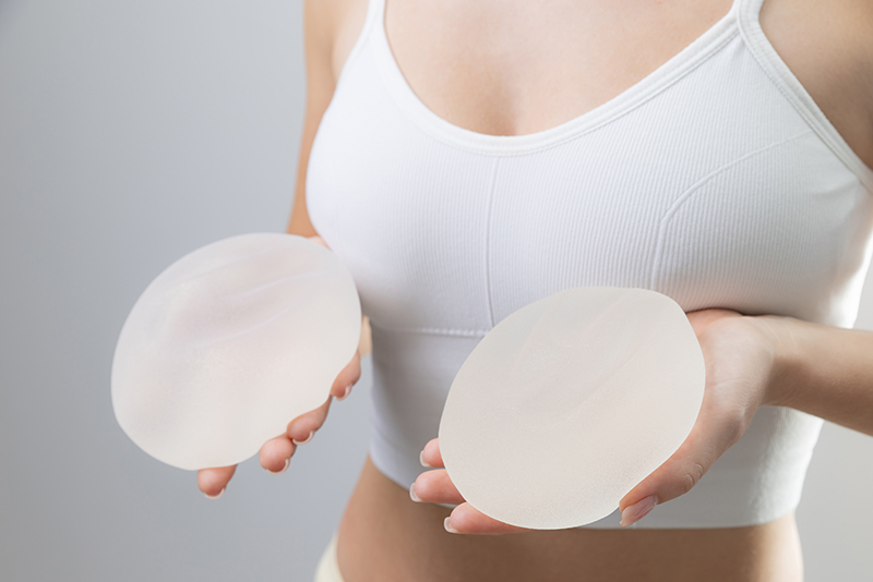 Woman in crop top holding round breast implants